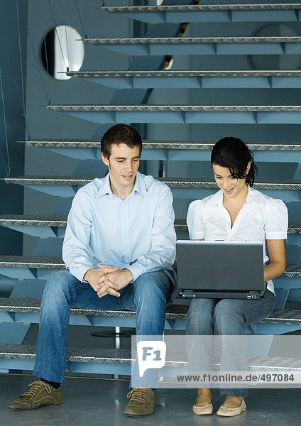 Zwei Kollegen im Gespräch  auf der Treppe sitzend mit Laptop