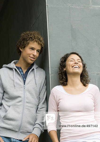 Junger Mann und Frau  die sich an die Wand lehnen und lachen.