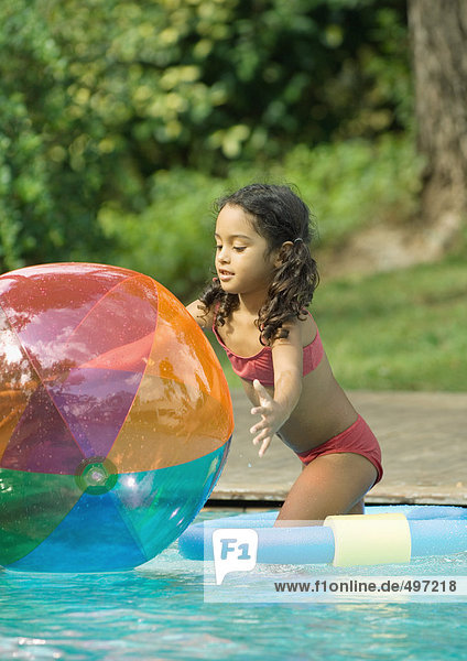 Girl standing in pool  reaching for beach ball