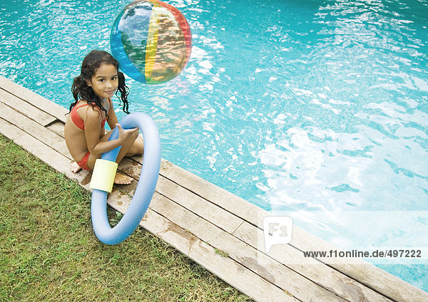 Girl sitting by edge of pool  holding floating ring