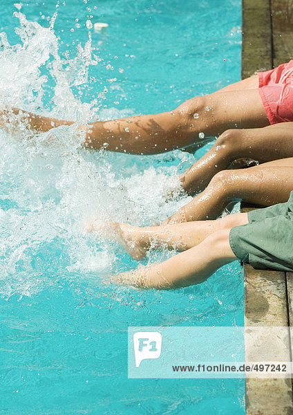 Man and children sitting on edge of swimming pool  splashing with legs