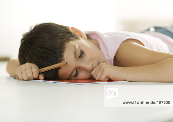 Kind beim Einschlafen mit Kopf auf Notebook und Bleistift in der Hand