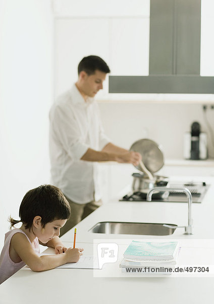 Kind macht Hausaufgaben auf der Küchenzeile  während Vater kocht.