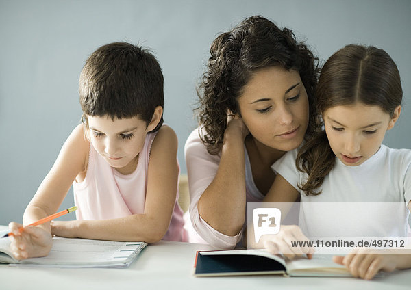 Junge Frau hilft Kindern bei den Hausaufgaben