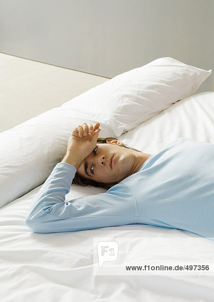 Mann auf dem Bett liegend mit Hand auf der Stirn