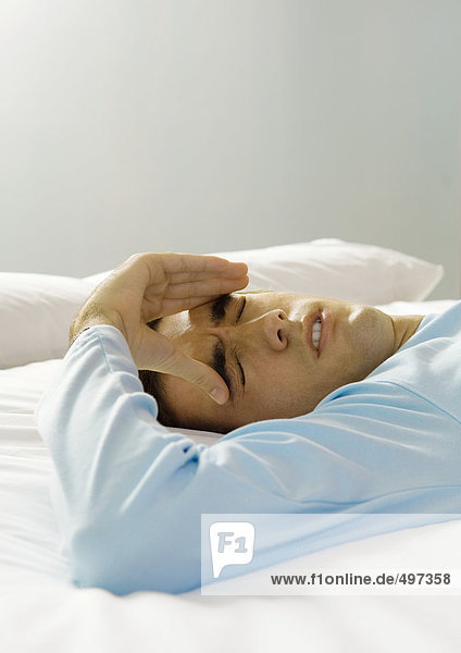 Man lying on bed with hand on forehead  making face