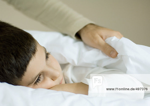 Kind im Bett liegend  Vater zieht Decken hoch