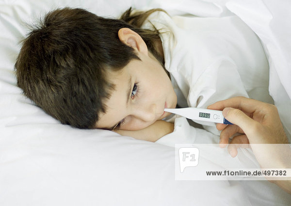 Kind im Bett liegend  mit Temperaturmessung