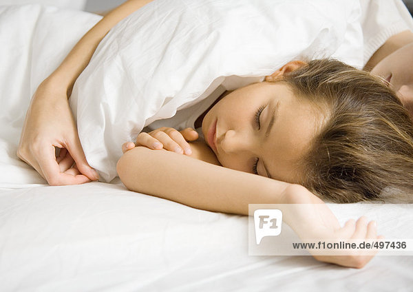 Girl lying in bed with mother's arm around her