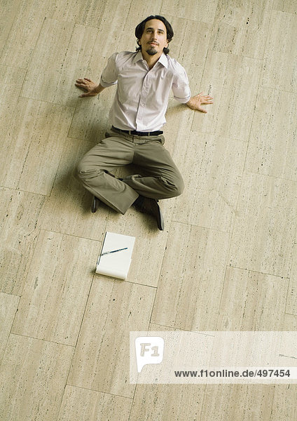Man sitting on floor with pad of paper in front of him  leaning back  high angle view