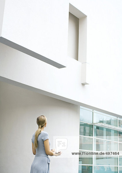 Frau steht  schaut auf die Fassade des Gebäudes  macht sich Notizen
