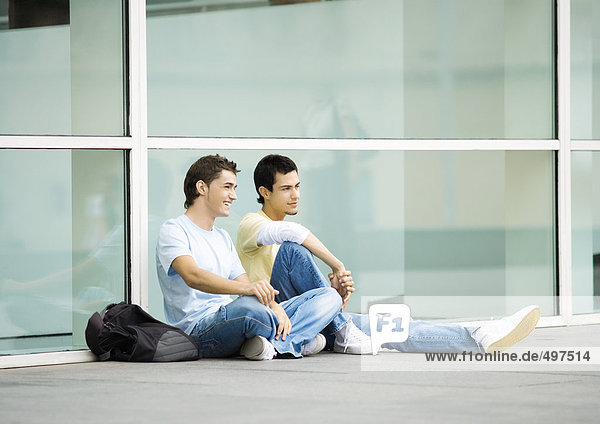 Two teenage boys sitting on ground in urban setting