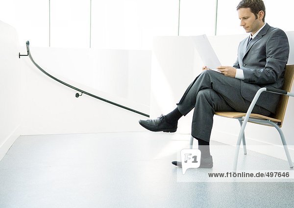Geschäftsmann sitzend auf Stuhl mit gekreuzten Beinen  Blick auf Dokument
