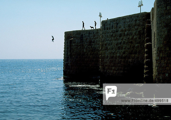 Menschen  die von der Steinmauer ins Meer springen.