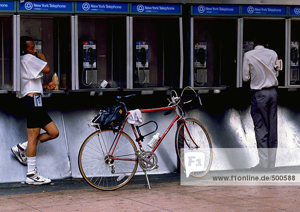 NY  NY  two men using pay phones  one with bike