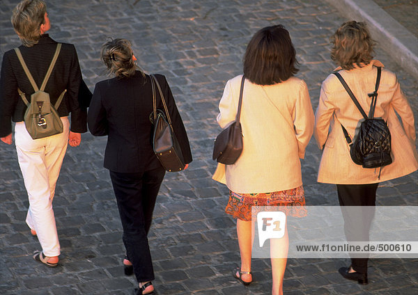 Four ladies walking on cobblestones  high angle  rear view.