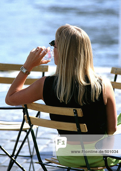 Frau sitzt im Freien im Stuhl und trinkt Wasser in Flaschen  Rückansicht.