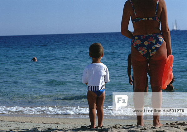 Mutter und Sohn am Strand stehend  Blick aufs Meer  Rückansicht