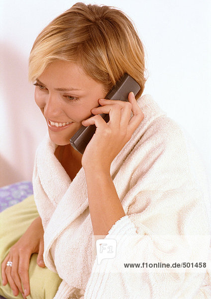 Woman in bathrobe talking on phone in bedroom.