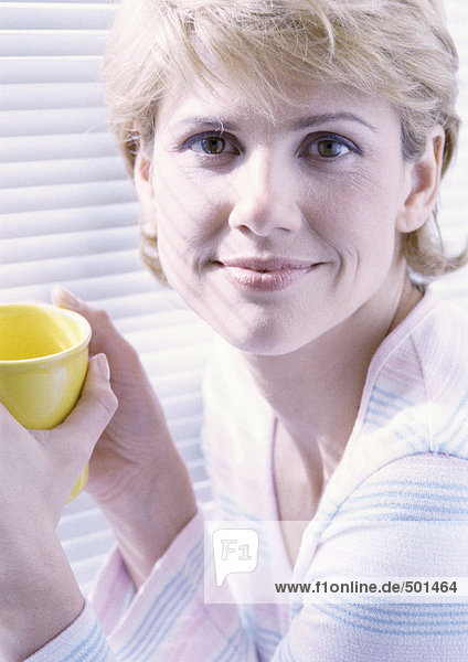 Frau mit Blick auf die Kamera  die eine Tasse in beiden Händen hält  Porträt.