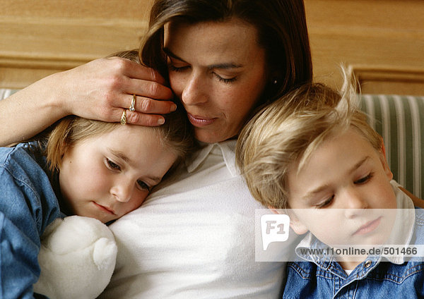 Frau zwischen zwei Kindern  hält den Kopf des kleinen Mädchens an die Brust  kleiner Junge lehnt sich an sie  Nahaufnahme