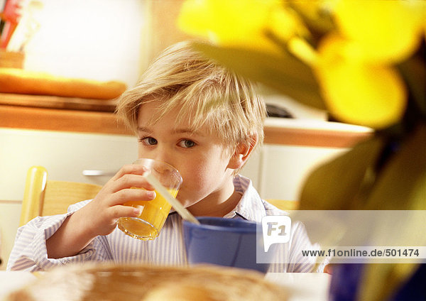 Kleiner Junge,  der bei Tisch Saft trinkt.