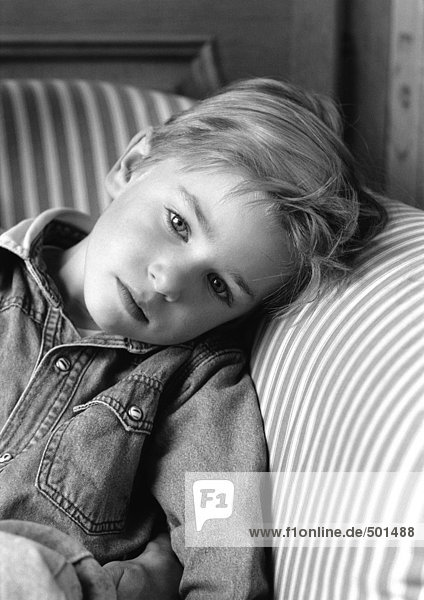 Kleiner Junge lehnt Kopf auf Stuhlarm,  schwarz-weißes Porträt.