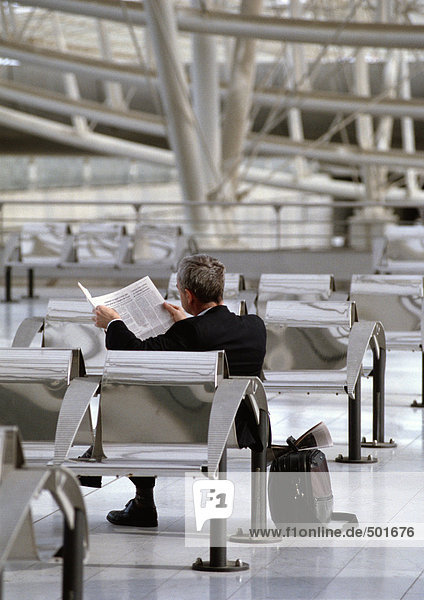 Geschäftsmann wartet am Flughafen  Zeitung lesen