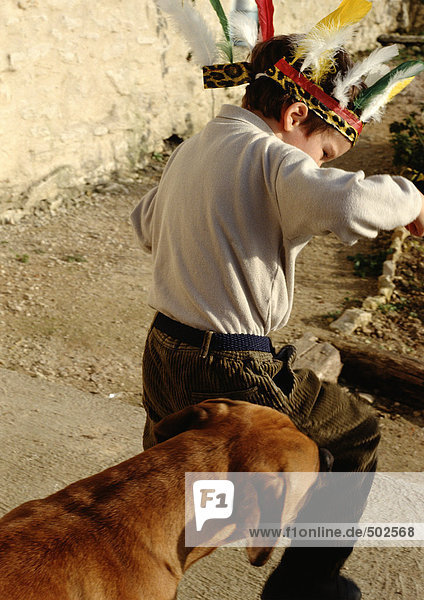 Junge mit Federkopfbedeckung  gefolgt von Hund  Rückansicht