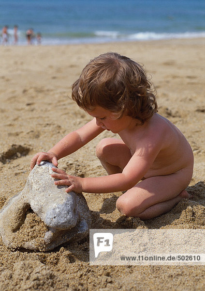 Nacktes Kind berührt Felsen am Strand