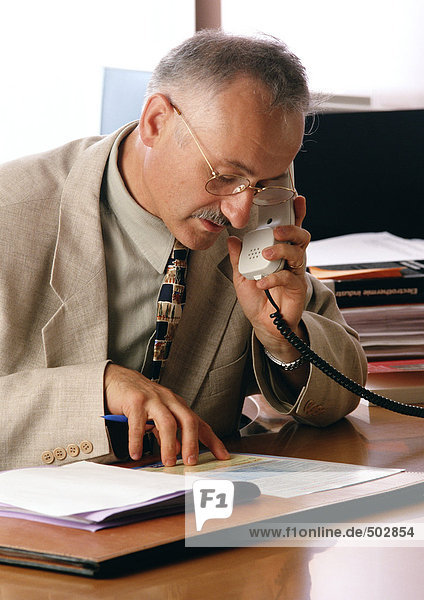 Mann sieht sich Dokumente an  während er das Telefon benutzt.