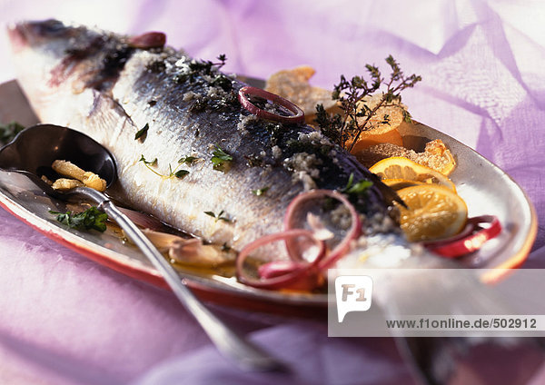 Whole cooked fish with citrus fruit and herbs on dish  close-up