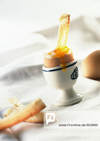 Weichgekochtes Ei im Eierbecher mit über die Seite tropfendem Eigelb und Brotkrusten