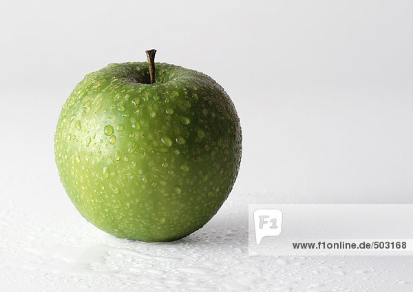 Grüner Apfel mit Wassertropfen bedeckt  Nahaufnahme  weißer Hintergrund.