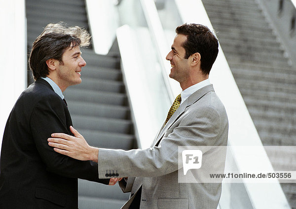 Two businessmen shaking hands in front of stairs