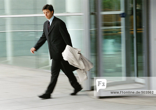 Businessman leaving building  holding overcoat  blurred