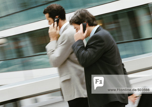 Two businessmen using cell phones outside  side view