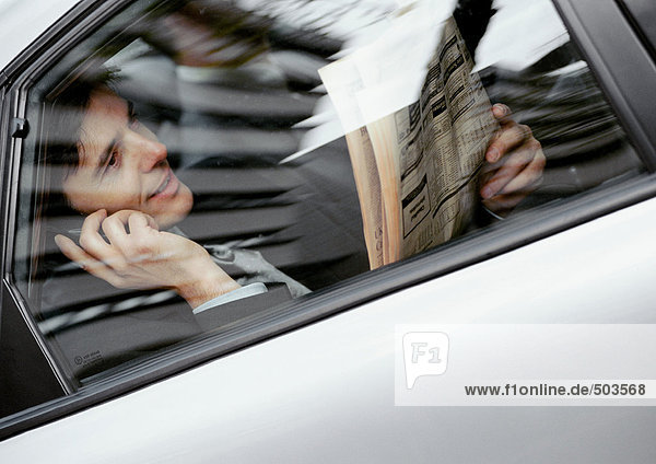 Geschäftsmann sitzt hinten im Auto  hält Zeitung und Handy  durchs Fenster gesehen