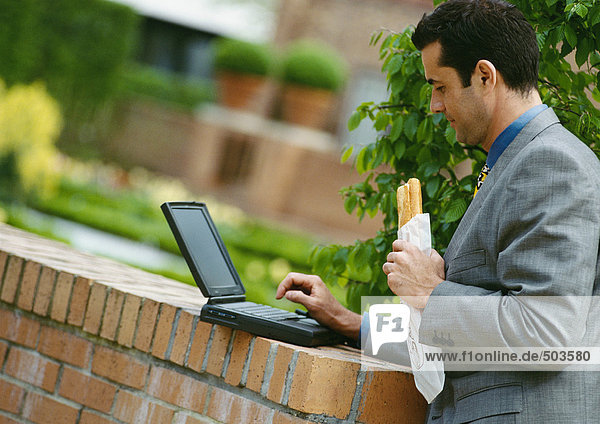 Geschäftsmann mit Laptop-Computer beim Essen Sandwich draußen
