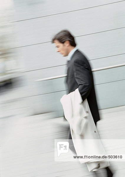 Businessman walking  holding overcoat  blurred