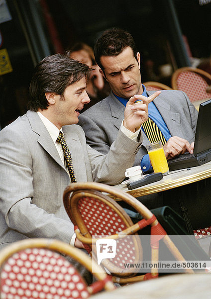 Zwei Geschäftsleute sitzen auf der Terrasse des Cafés und schauen auf den Laptop.