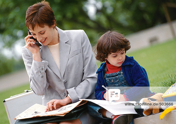 Geschäftsfrau und Kind sitzen draußen zusammen  Frau mit Handy