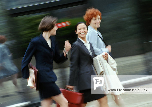 Three businesswomen walking in street  smiling  blurred