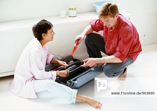 Man and woman with toolbox between them on floor  full length