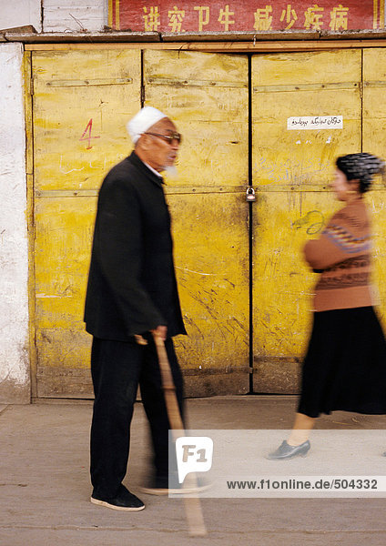 China  Provinz Xingjiang  Turpan  älterer Mann  der mit dem Stock an einem geschlossenen Restaurant vorbeigeht.