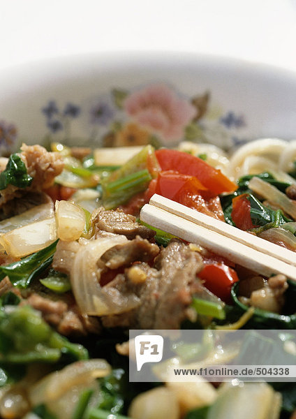 Chopsticks on dish of meat and vegetables  close-up