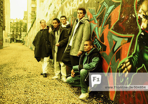 Fünf junge Männer  die sich an eine mit Graffiti bedeckte Wand lehnen  volle Länge