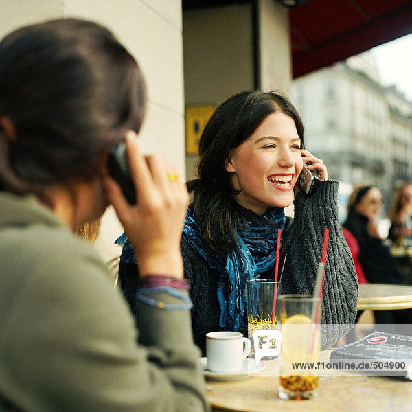 Zwei Teenager-Mädchen sitzen auf der Café-Terrasse und halten Handys.