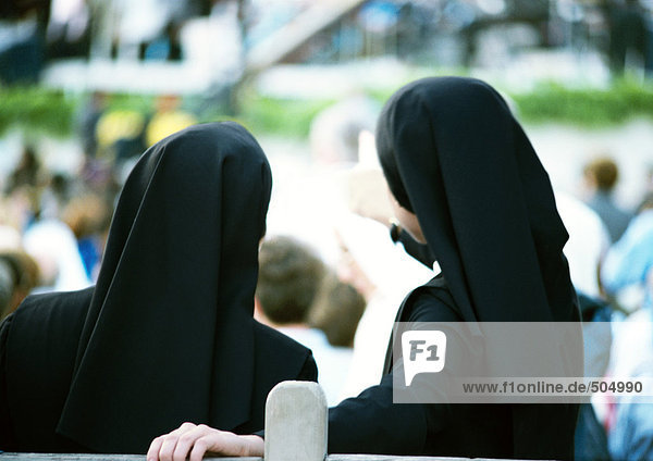Two nuns standing side by side  overlooking crowd  rear view