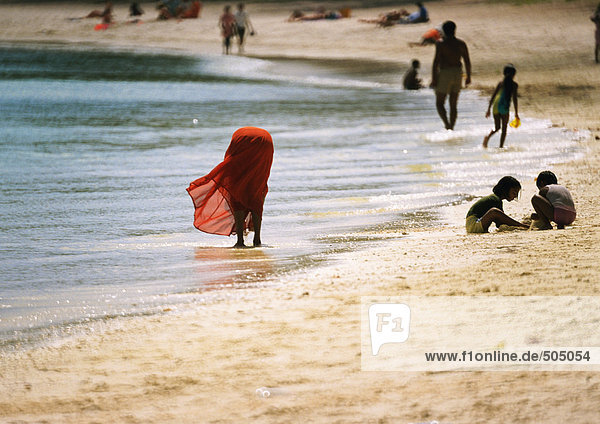 Menschen am Strand  Frau bückt sich  knöcheltief im Wasser